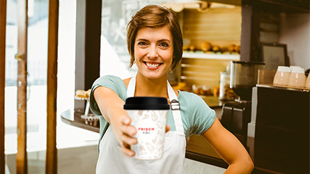 Bäckereifachverkäuferin reicht Coffee-to-go-Becher Bäckereifachverkäuferin reicht Coffee-to-go-Becher