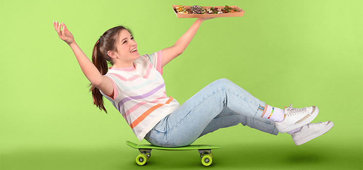 Une dame roule sur un skateboard avec un plateau de restauration à la main.