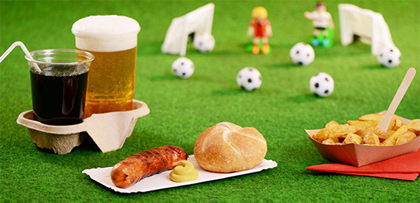 Wurst mit Brötchen, Pommes und Getränk auf grünem Rasen