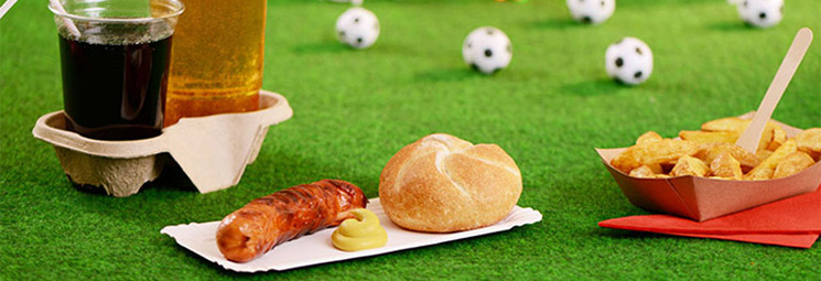 Wurst mit Brötchen, Pommes und Getränk auf grünem Rasen